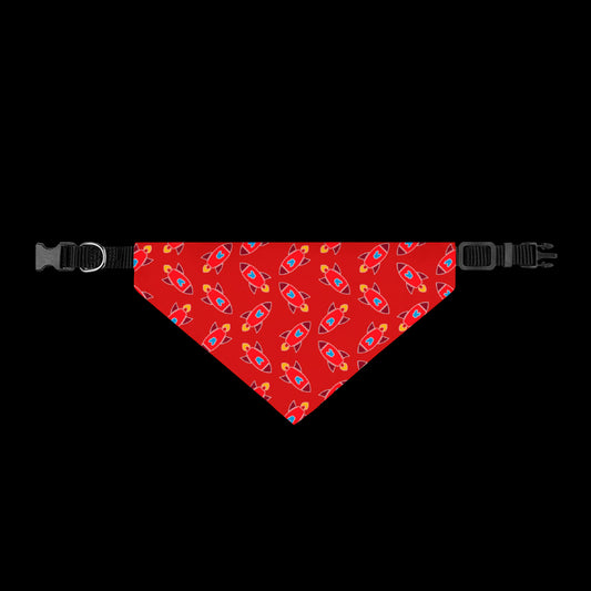 A red pet bandana with a repeating pattern of colorful rockets, shown flat with black plastic buckles on both ends.