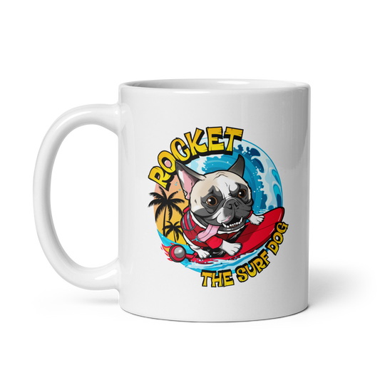 A white ceramic coffee mug featuring a colorful cartoon graphic of a French bulldog surfing on a red board, with the text 'ROCKET THE SURF DOG' in yellow.